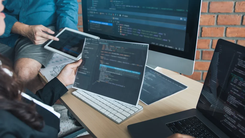A person viewing and discussing code on multiple devices, focusing on web development.